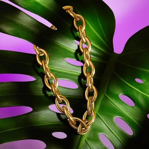 צילום תכשיטים מקצועי של שרשרת זהב גדולה מונחת על עלה מונסטרה צבעוני, ליצירת קומפוזיציה טבעית ואלגנטית