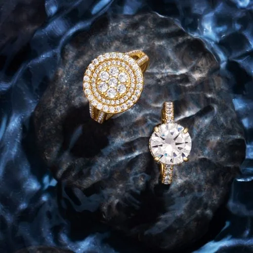 צילום תכשיטים מקצועי של שתי טבעות זהב מדהימות עם יהלומים עגולים גדולים, על רקע מים כהים נוצצים ליצירת סצנה אלגנטית