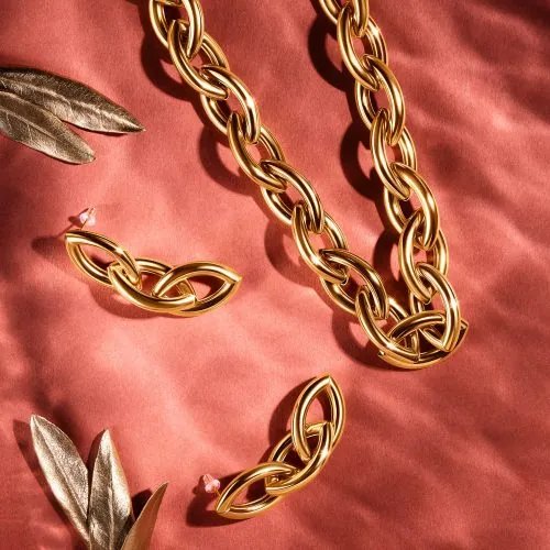 שרשרת ועגילים מזהב בתצוגה צבעונית עם עלי זהב, מוצגים על משטח אדום בצילום תכשיטים מקצועי